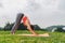 Slim curly woman standing in downward dog pose on green grass