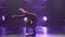 Slim cute attractive girl athlete in burgundy swimsuit performs elements of rhythmic gymnastics in dark studio with