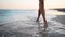 Slim female legs and feet walking along sea water waves on sandy beach. Pretty woman walks at seaside surf. Splashes of
