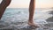 Slim female legs and feet walking along sea water waves on sandy beach. Pretty woman walks at seaside surf. Splashes of