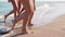 Slim female legs and feet walking out of sea water waves on sandy beach. Pretty women move on seafront. Splashes of