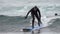 Slim female surfer in hooded wetsuit rides wave in Pacific Ocean on Kamchatka Peninsula. Slow motion shot