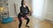 Slim fit sportswoman squatting indoors using resistance band. Portrait of confident slender Caucasian woman exercising