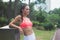 Slim fitness brunette woman with six pack abs wearing pink sport bra standing in city park relaxing after workout