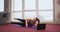 Slim, flexible, brunette girl lying on back on yoga mat, raising legs, meditating.