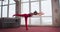 Slim, flexible girl training, stretching, meditating at home, wearing red top and leggings.