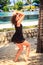 slim girl in black barefoot poses against pool and umbrellas