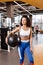 Slim girl with dark curly hair dressed in a sportswear is standing with heavy fitness ball in the modern gym with big