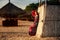 slim girl in long and big red hat leans on reed wall on beach