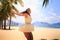 slim girl in white backside view poses with hands up on beach