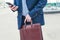 Slim man in a suit tucks his shirt in his pants while calling by phone on the street.