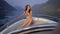 Slim pretty girl dressed in bikini is sitting on yacht in sunny day during sea walk near shore with mountains