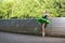 Slim Sensual Winsome Sexy Relaxed Professional Caucasian Ballet Dancer in Green Tutu Dress Posing Near Stony Fence Against Green