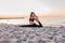 Slim strong young woman in black practicing yoga doing the splits on sand beach close-up with copy space. Sunset, summer. Healhy