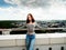 Slim teenager girl posing on top of a building with beautiful town in the background. Travel and tourism concept. Cloudy sky.