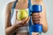 Slim unrecognizable woman with tape measure holding blue dumbbells and apple.