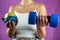 Slim unrecognizable woman with tape measure holding blue dumbbells and apple.