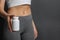 Slim woman holding bottle of weight loss pills against gray background, closeup