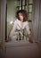 Slim young fashion model wearing white coat in window frame. Lovely fashionable woman with light brown curly hair