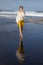 Slim young woman walking on black sand beach. Caucasian woman wearing yellow sportswear and white blouse. Happiness and freedom.