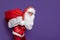 slinking santa claus carrying huge bag of gifts on color background while looking at camera.