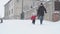 Slo-mo authentic happy young man dad in black with baby son run down on snowy road. Snowfall in cold season weather in