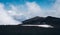 The slope of Mount Etna covered with dried lava, snow and clouds above it