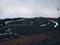 The slope of Mount Etna covered with dried lava, snow and clouds above it