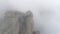 Slope of mountain in mist. Shot. Dense gray fog envelops entire space. Top view of rock plunging into cold autumn fog