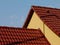 Sloped clay roof ridge. red roof tiles and yellow attic wall under clear blue sky