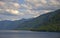 The slopes of the mountains are forested on the shore of a mountain lake under thunderclouds