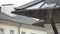 The sloping roof of the house and the falling raindrops close-up. Rainwater flowing down the metal roof and downpipe. Heavy rain