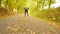 Slow camera movement. Sportsman in black sortswear run on road. The man is slowly running on asphalt way covered by autumn leaves