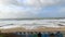 A slow-mo footage of a storm at the beach with rough water crashing wave on a sandy beach along a promenade with beach huts under