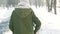 Slow motion back view of woman in warm winter clothes walking in snowy winter city park at frozzy sunny day.