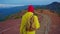 Slow motion camera follows woman hiker in yellow raincoat with backpack. Attractive happy young girl with backpack