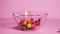 Slow motion of candies falling into glass bowl on pink background. Multicolored delicious candy balls