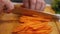 In slow motion, a chef professionally slices carrots with a knife. Side view. Close-up. The concept of tasty and healthy