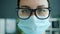 Slow motion close-up portrait of serious lady medic in mask and glasses in office