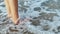 Slow motion closeup barefoot female legs on beach with rolling waves.