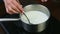 Slow motion closeup female hand by spoon stirs hot milk in metal saucepan