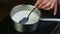 Slow motion closeup female hand by spoon stirs milk boiling in metal saucepan