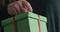Slow motion closeup female hands holds and opens green paper gift box with red ribbon bow