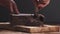 Slow motion closeup young man hands cutting dark chocolate block with parmesan knife on wood board