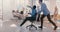 Slow motion crazy fun young black businessman riding office chair, celebrating success with team throwing paper in air.