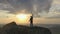 Slow motion drone footage of a young happy male climber standing on top of a mountain successfully raising his arms and