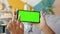 Slow motion of girl\'s hands touching green vertical smartphone screen indoors