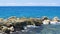 Slow motion. Gorgeous view of waves breaking on stones. Turquoise water of Atlantic ocean and big rocks on blue sky background.