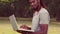 In slow motion handsome hipster using laptop in the park