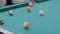 Slow motion: hitting pool ball on teal billiards table - close up